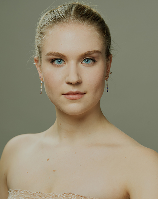 Photo color enhancement service of a young woman with blue eyes, braided hair, dangling earrings, and off-shoulder dress.