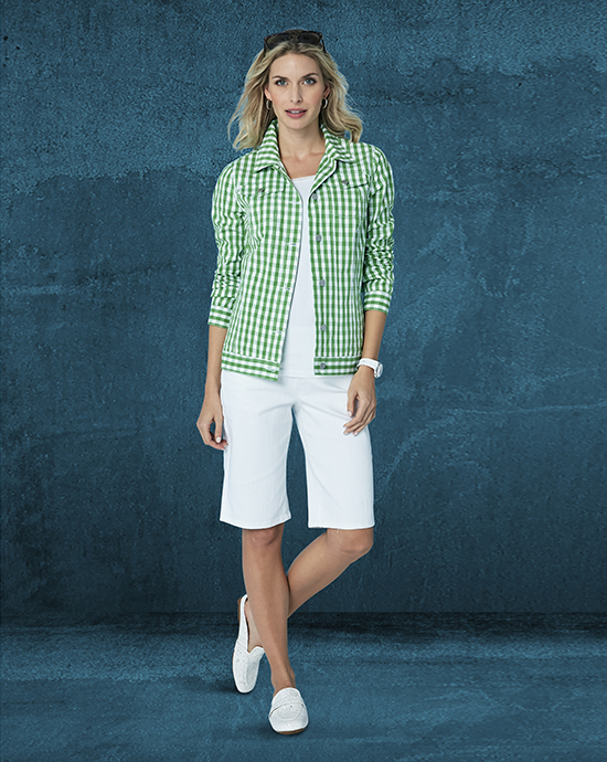 A woman in a green and white checkered jacket and white shorts against a textured blue background.