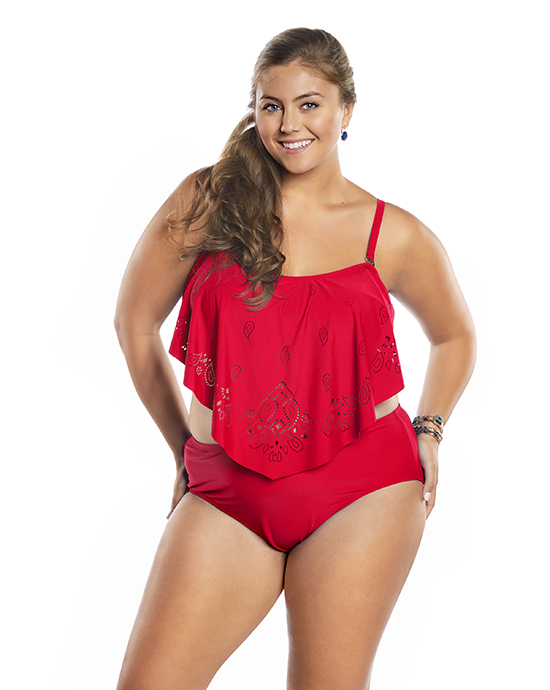 A young woman in a red patterned tank top and matching shorts poses with a confident smile against a white background.