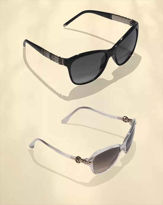 Two pairs of sunglasses, black and white, on a light beige background with visible shadows.