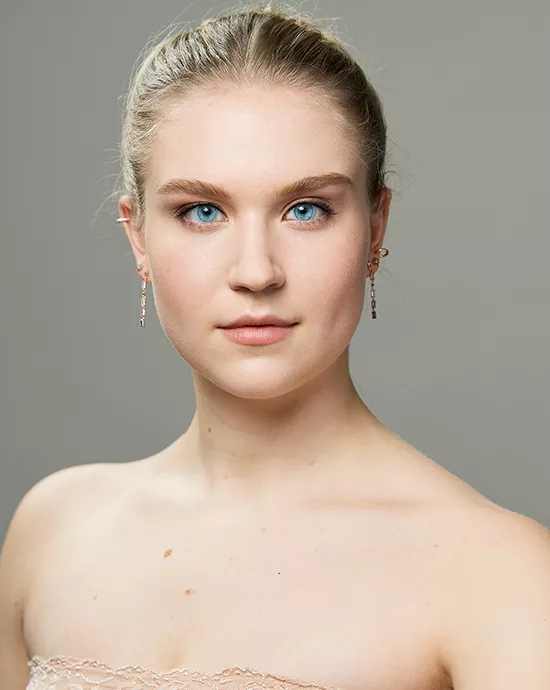 Photo color enhancement service of a young woman with blue eyes, blond hair, lace dress, and earrings on a gray background.