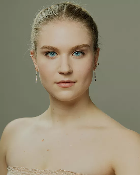 Photo color enhancement service of a young woman with blue eyes, braided hair, dangling earrings, and off-shoulder dress.