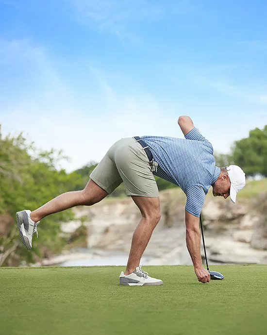 Man in a playful pose picking up a golf ball on a sunny golf course.