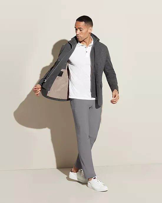 Man walking in casual outfit: grey coat, white polo shirt, grey trousers, and white sneakers.