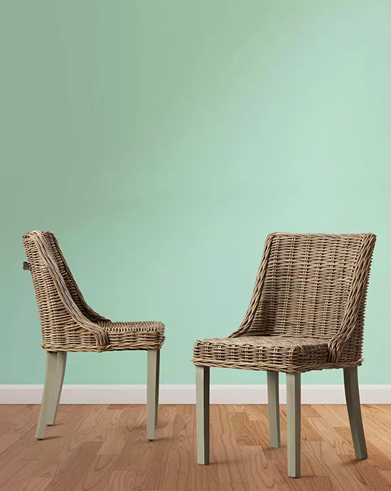 Background removal services for two wicker chairs against a mint green wall on a wooden floor.