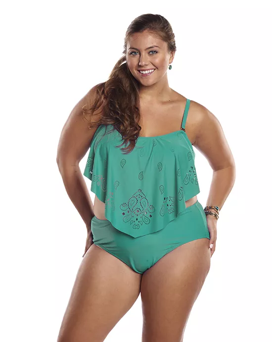 A smiling woman in an aqua tankini with printed details, standing against a white background.