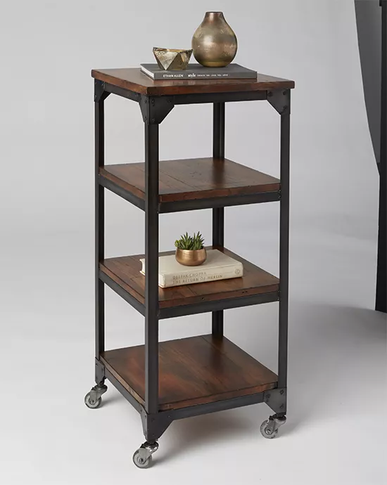 Industrial-style wooden shelving cart on wheels, with decor items on the shelves, against a light background.