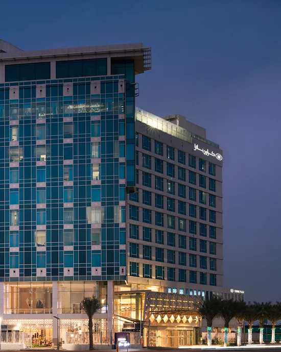 Twilight view of modern high-rise hotel with blue glass facade and ground level shops.