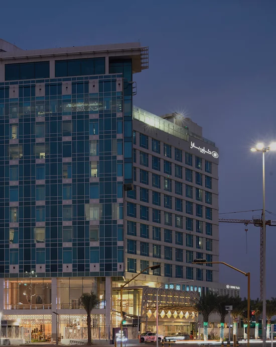 Modern high-rise buildings with illuminated facades by roadside during twilight.