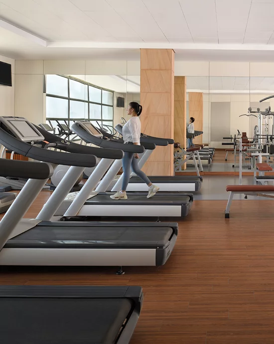 Modern gym with individuals on treadmills and workout equipment in bright wood-paneled room.