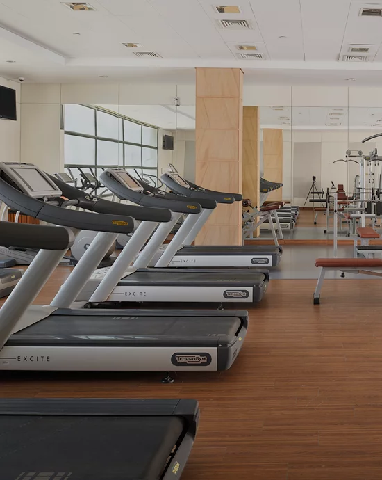 Well-lit gym with treadmills in foreground and exercise equipment in background.