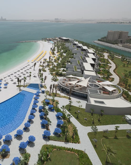 Aerial view of luxury beachfront resort with pools, umbrellas, and landscaped gardens.