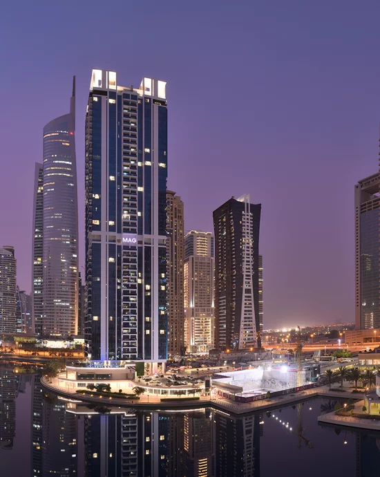 Twilight view of modern skyscrapers reflecting lights on calm waterfront.
