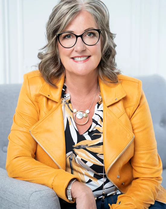 Mature woman smiling in yellow leather jacket, glasses – Professional photo retouching services.