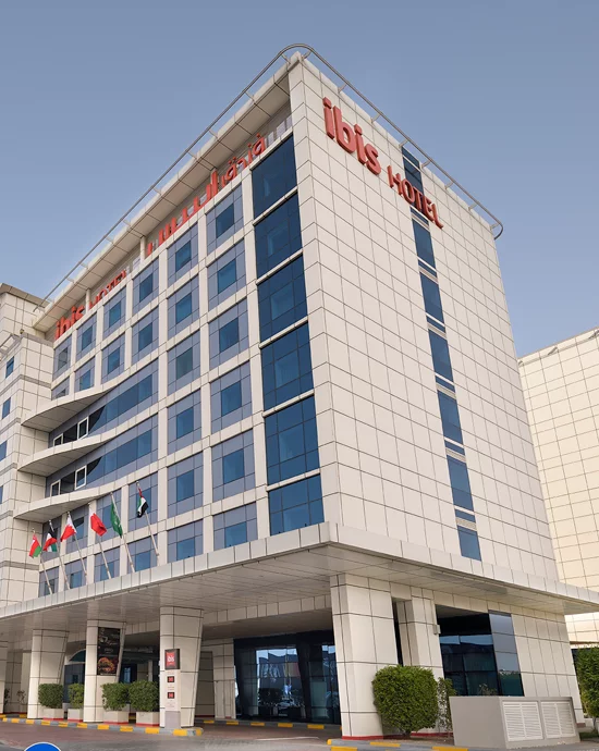 Modern multi-story Ibis hotel with glass facade and national flags at entrance.