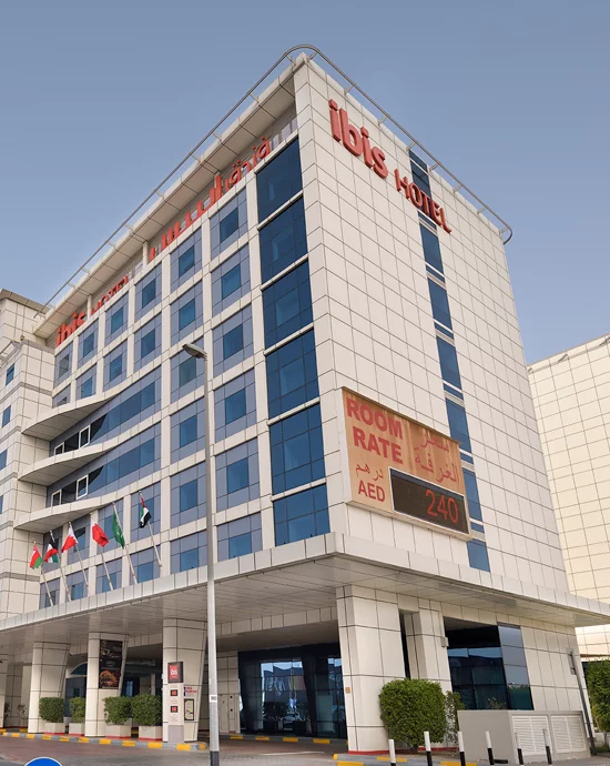 Modern Ibis Hotel exterior with digital room rate sign displaying AED 240 and flags.