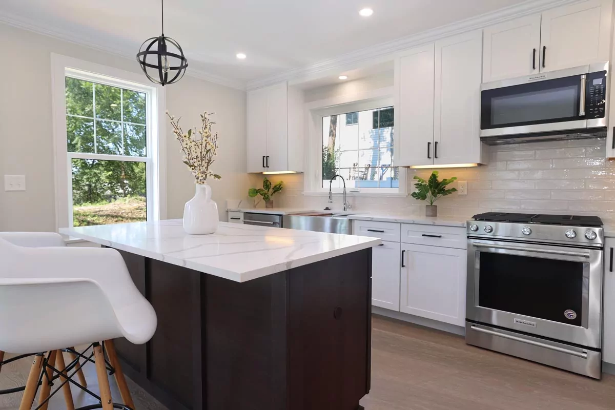 Bright kitchen with white cabinets, stainless steel appliances, marble island, and modern decor with natural light.