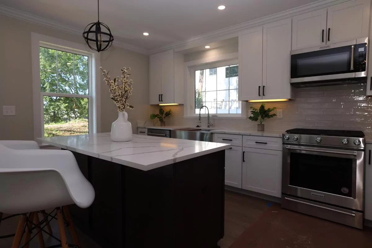 Modern kitchen with marble island, stainless steel appliances, white cabinets, and a window showing greenery outside.