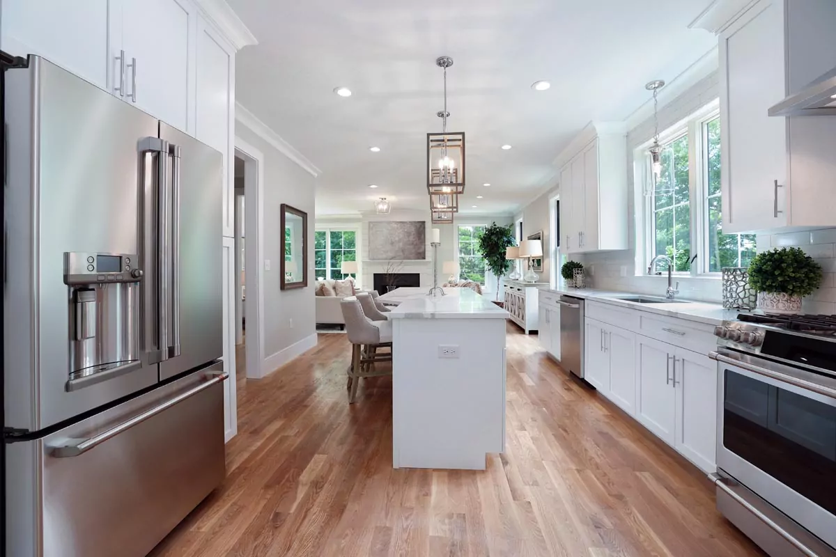 Modern kitchen with stainless steel appliances, white cabinets, spacious island, and hardwood floors in natural light.