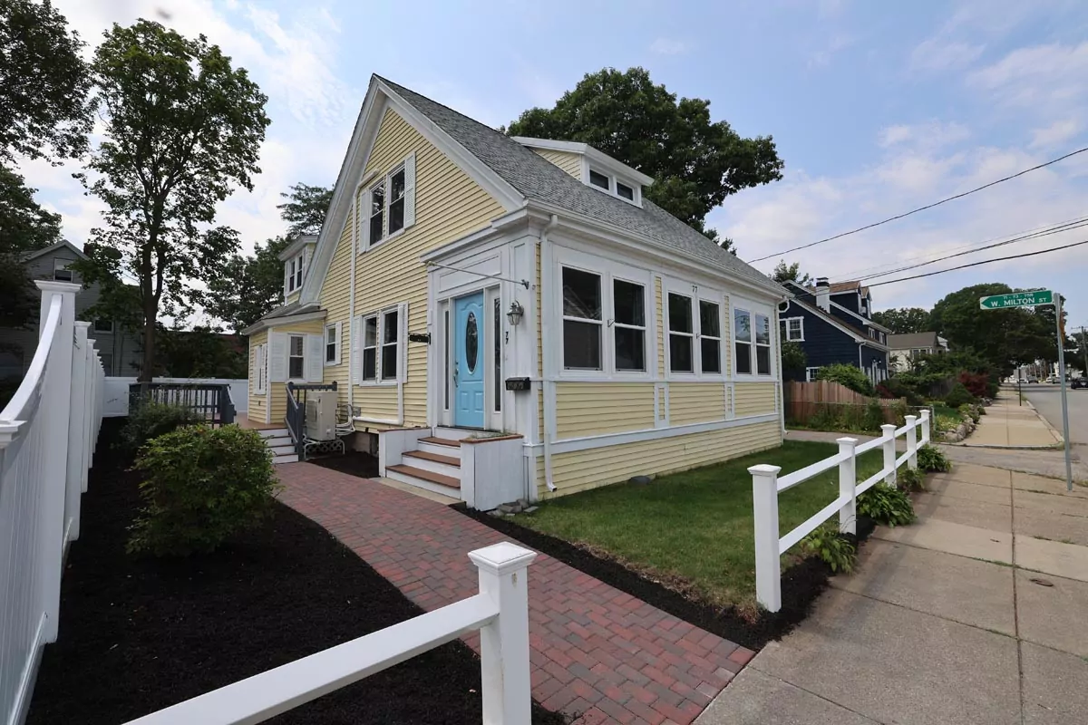 Charming yellow house with white trim and blue door, landscaped yard, sidewalk, under a partly cloudy sky.