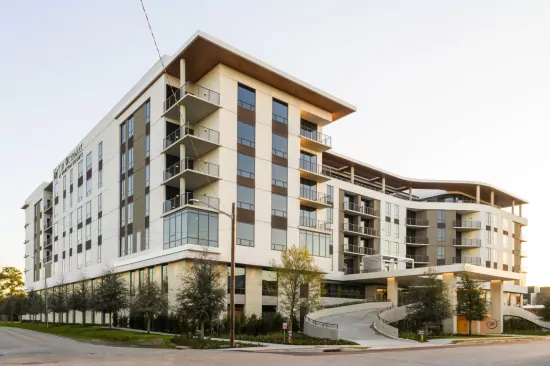 5_before Modern multi-story residential building with balconies, large windows, and landscaped entryway against a clear sky.