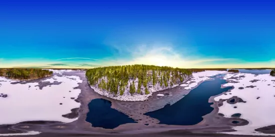 Panoramic snowy landscape with a green island surrounded by blue water under clear sunrise sky.