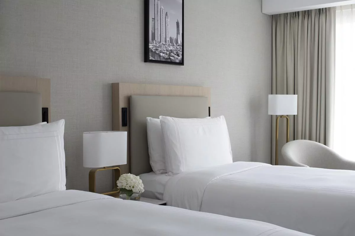 Modern hotel room with twin beds, sleek lamp, chair, and skyline photo for Real Estate Photo Editing Services.