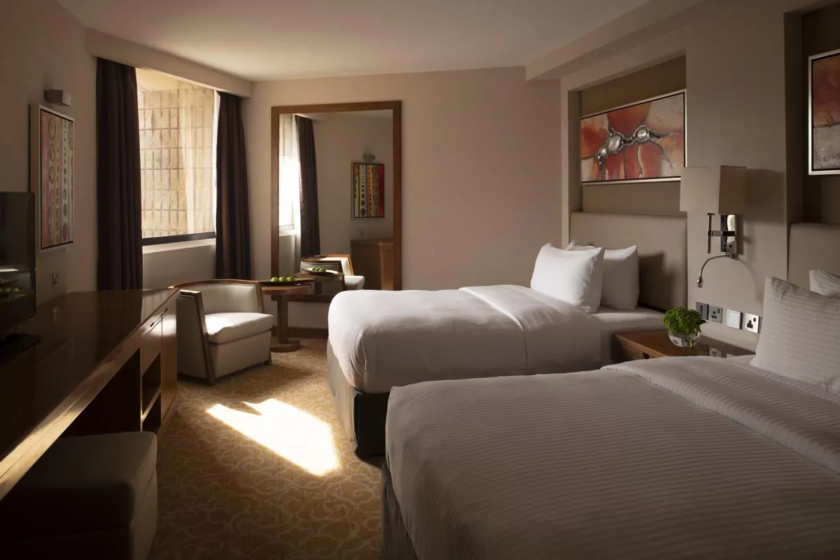 Cozy hotel room with two beds, desk, seating area, and large window for Real Estate Photo Editing Services.